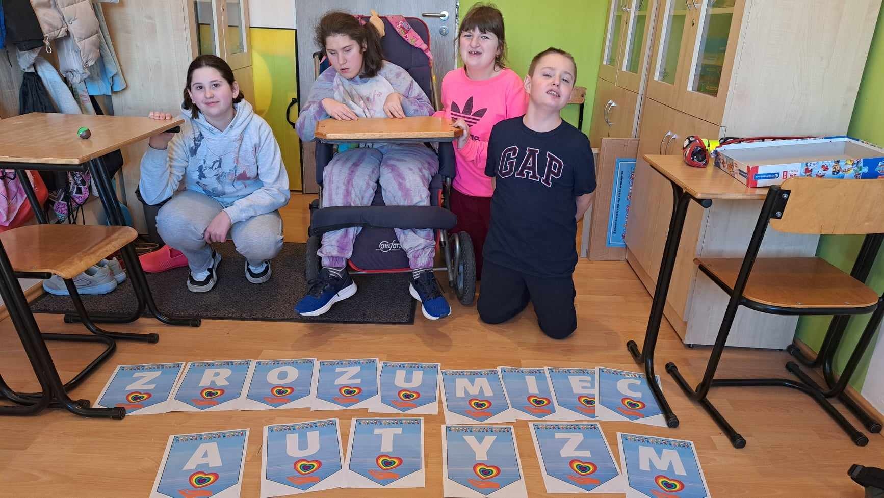 4 uczniów , w tym 1 dziewczynka na wózku pozują do zdjęcia z napisem: zrozumieć autyzm