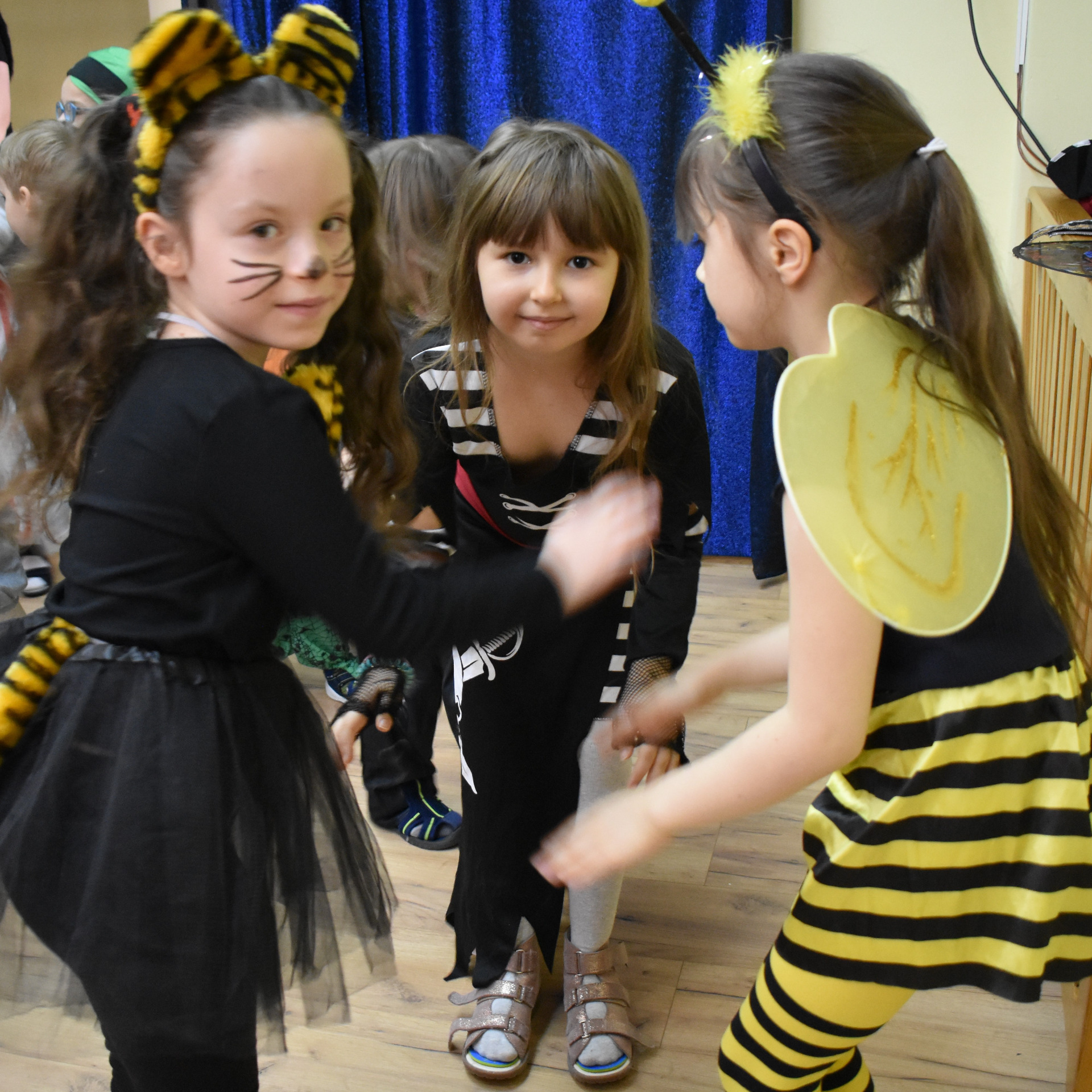 Trzy dziewczynki z najstarszej grupy tańczą w strojach tygrysa, piratki i pszczółki na balu karnawałowym.