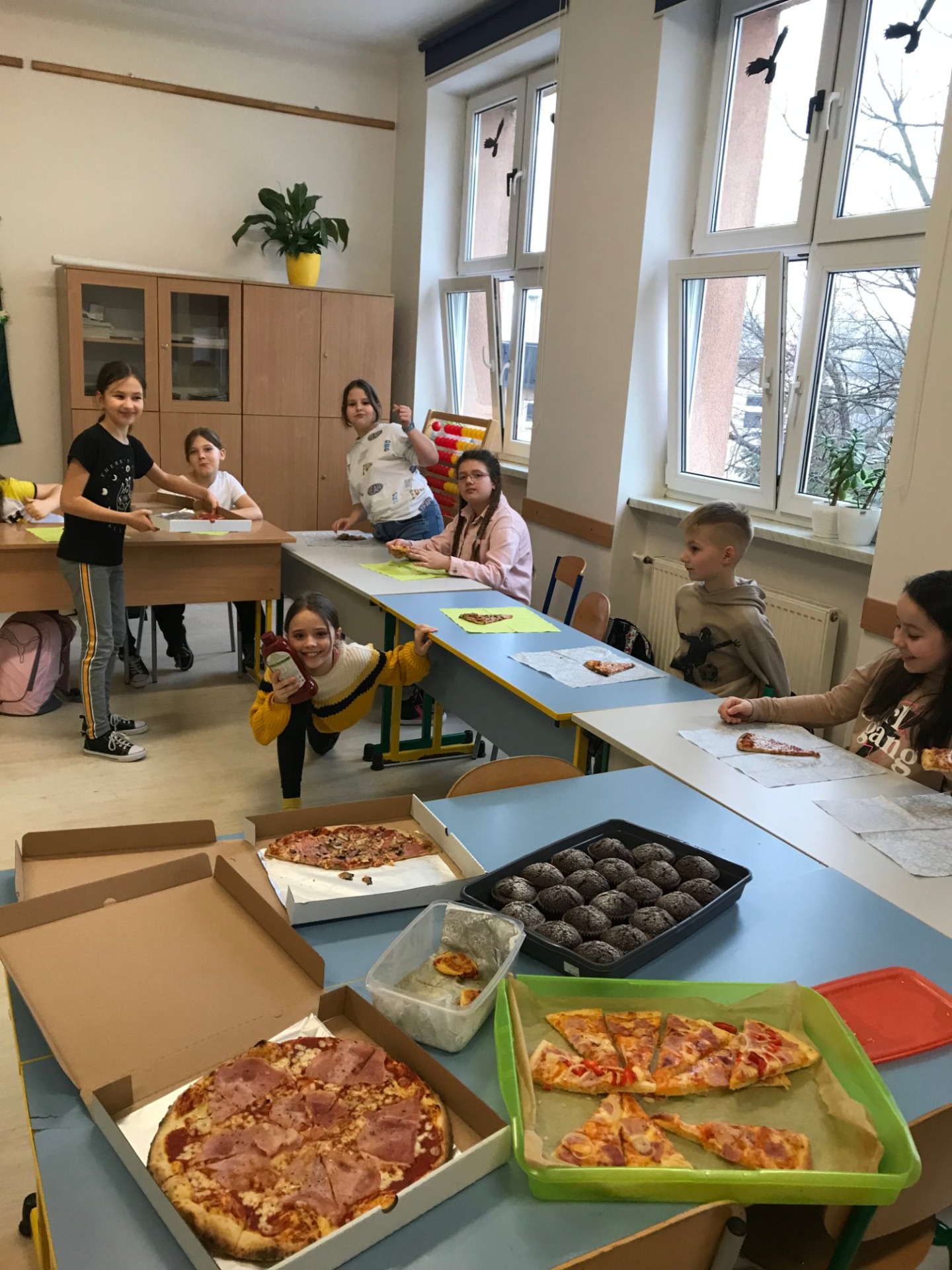 Grupa dzieci siedząca przy stole podczas poczęstunku pizzą
