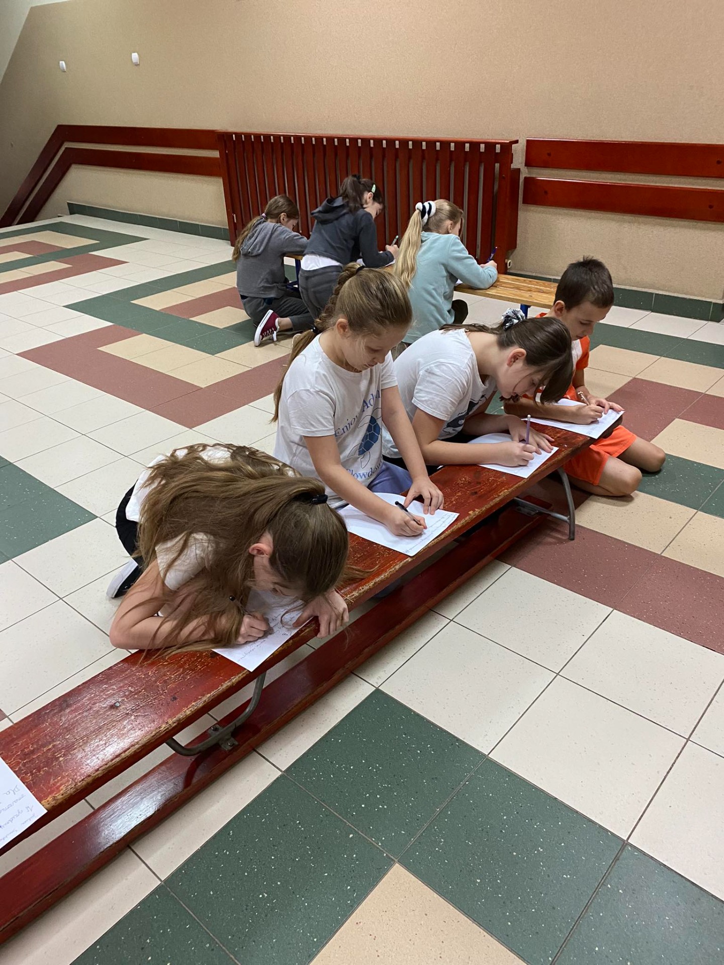 Uczniowie piszą dyktando na ławce na szkolnym korytarzu