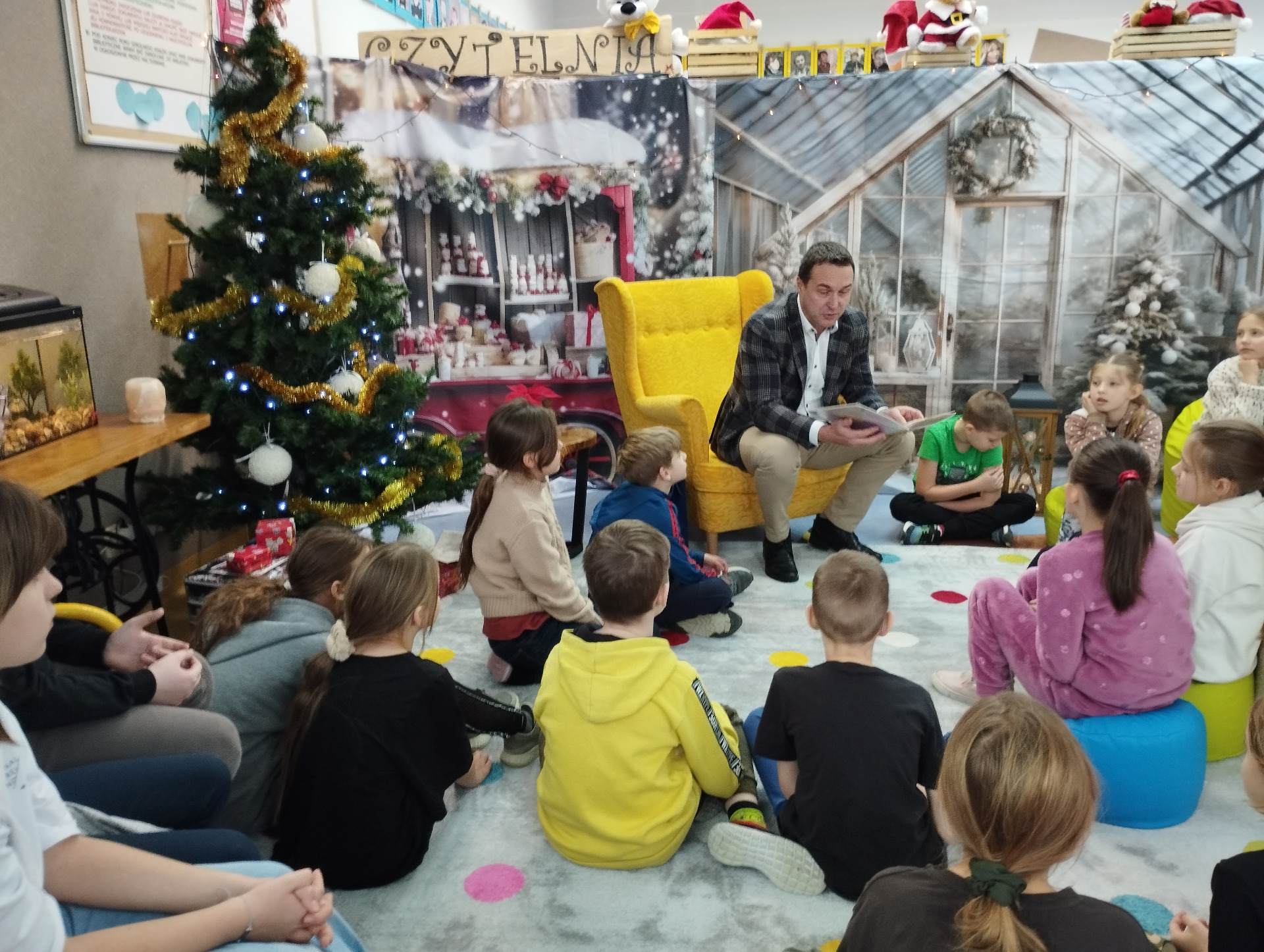 Burmistrz Tychowa siedzi w fotelu i czyta książeczkę uczniom klas trzecich
