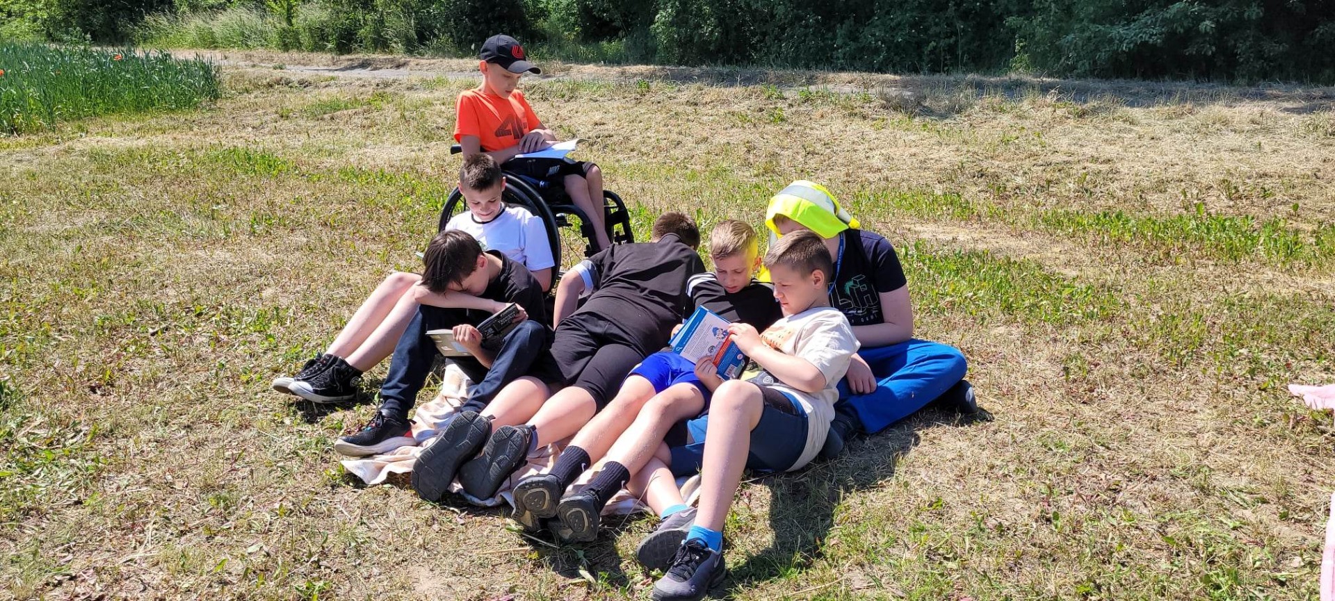 Uczniowie czytają książki na kocach na świeżym powietrzu.