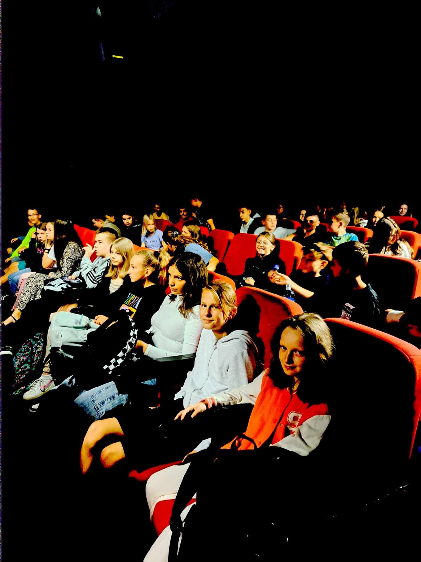 Chłopcy i dziewczęta siedzą w sali kinowej.