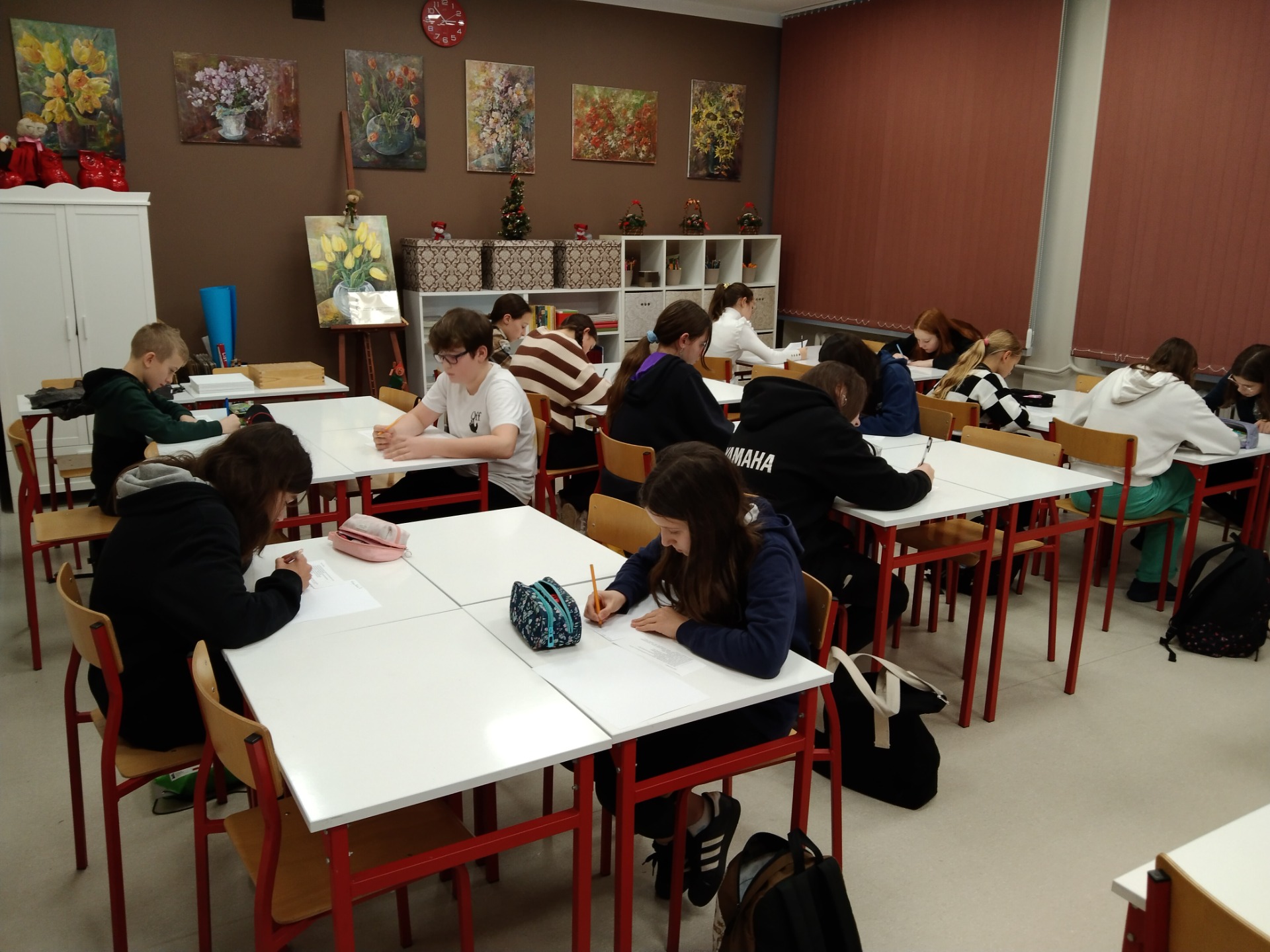 zdjęcie przedstawia uczniów, którzy siedzą przy ławkach i piszą prace literackie na kartkach