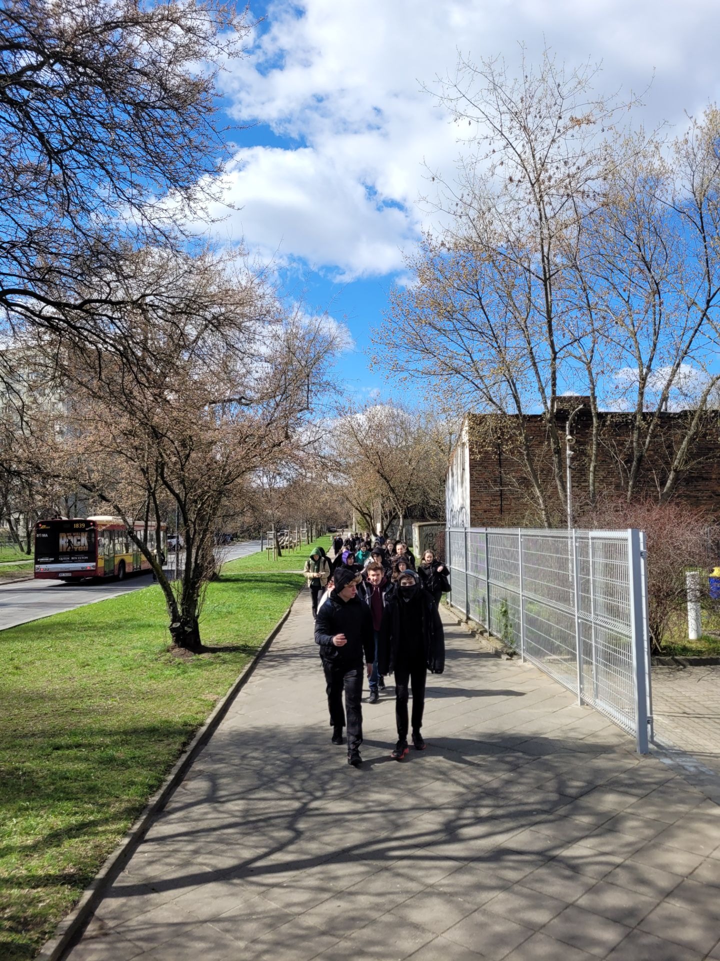 W drodze do muzeum; grupa uczniów idzie chodnikiem, jest ładna  pogoda. 