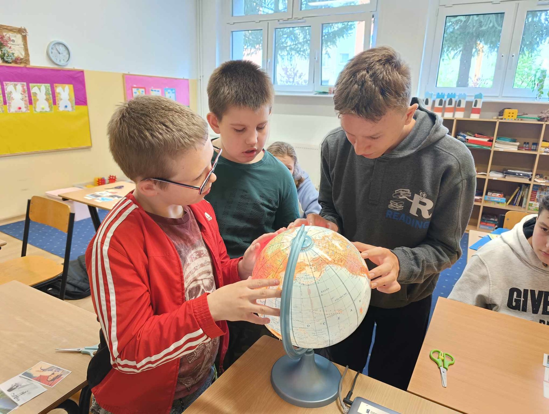 Uczniowie klasy 4 oglądaja model kuli ziemskiej - globus