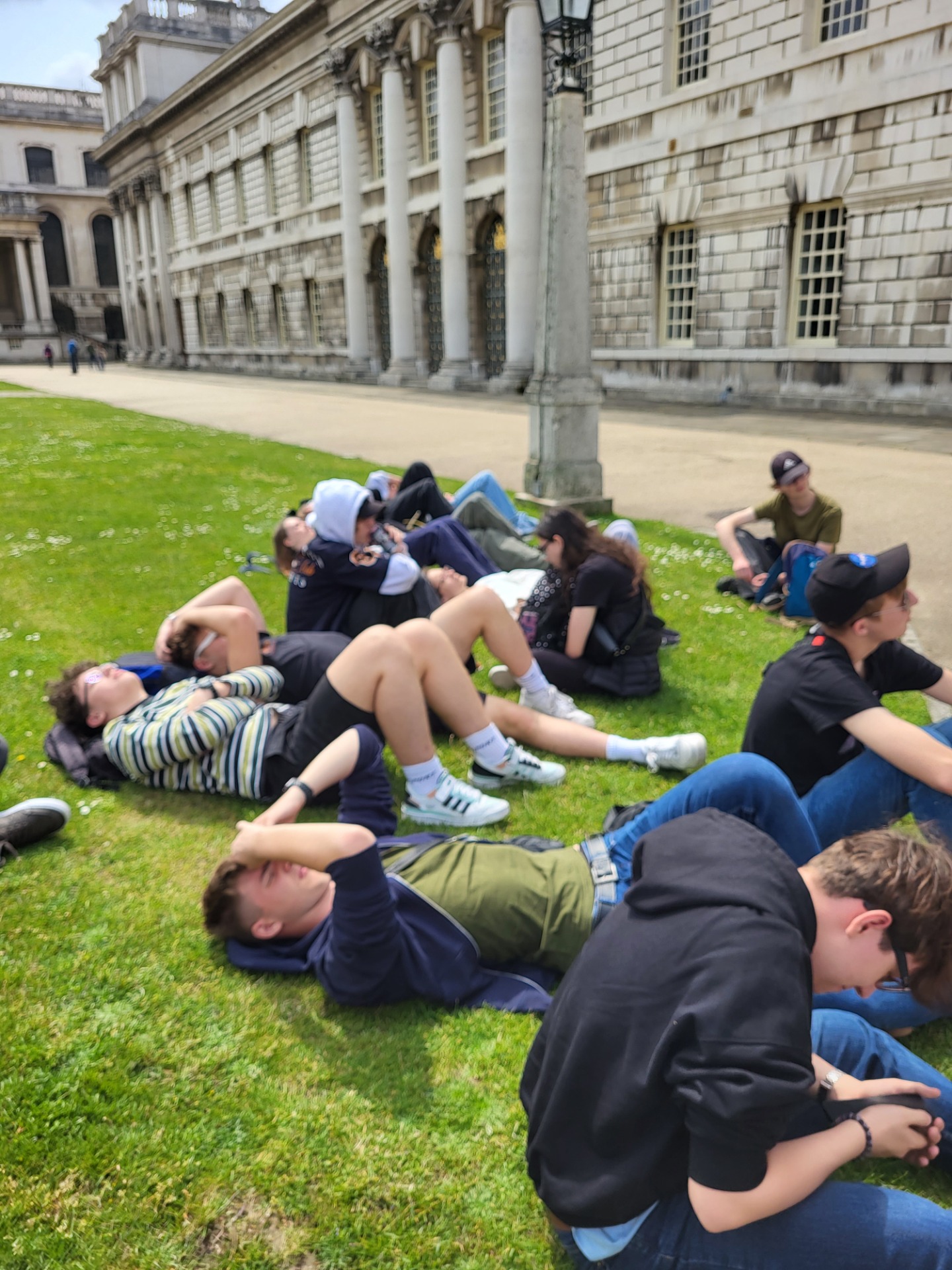 Uczniowie odpoczywają leżąc na trawie. 