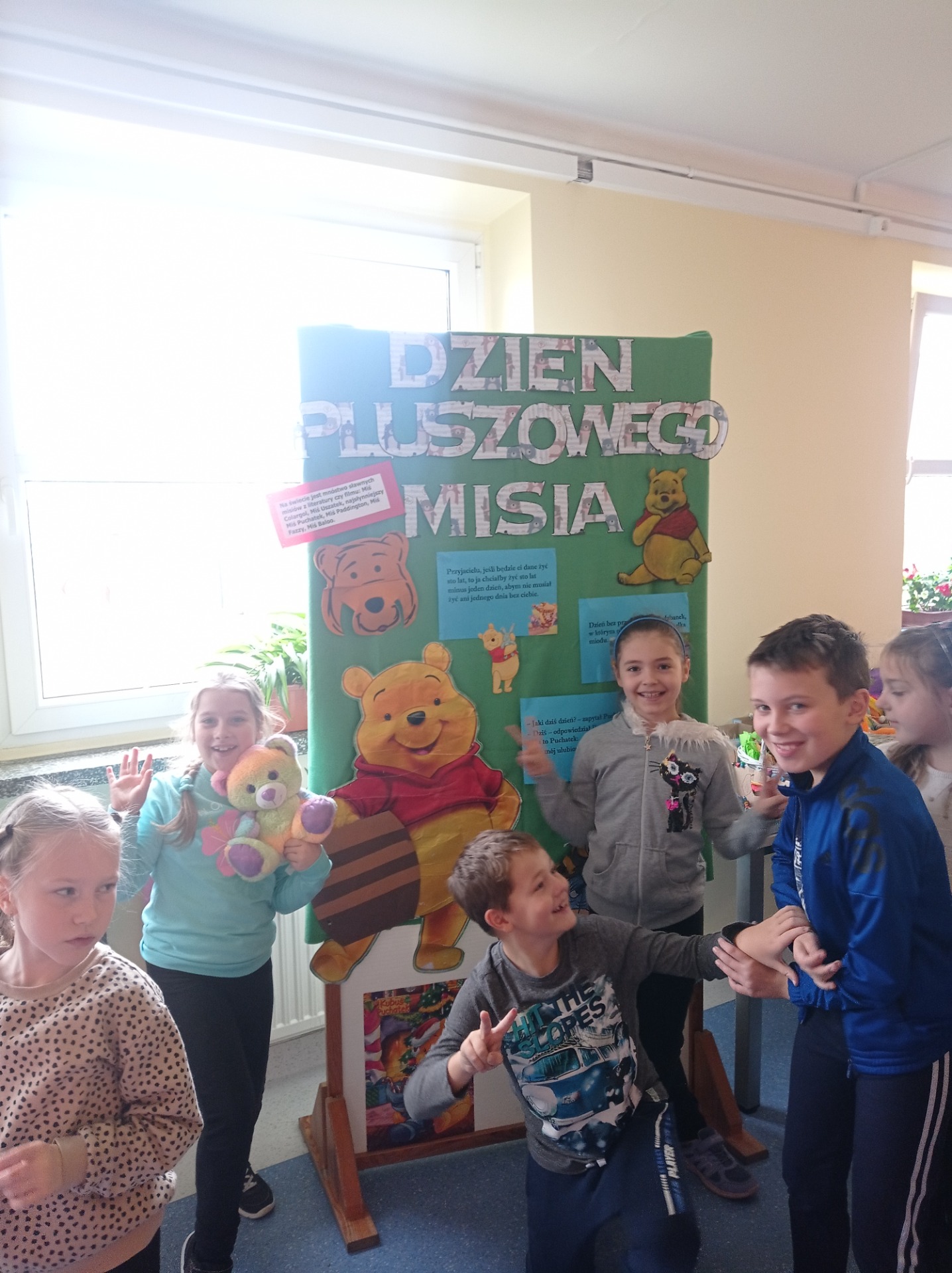 Dzieci na tle plakatu Dzień Pluszowego Misia