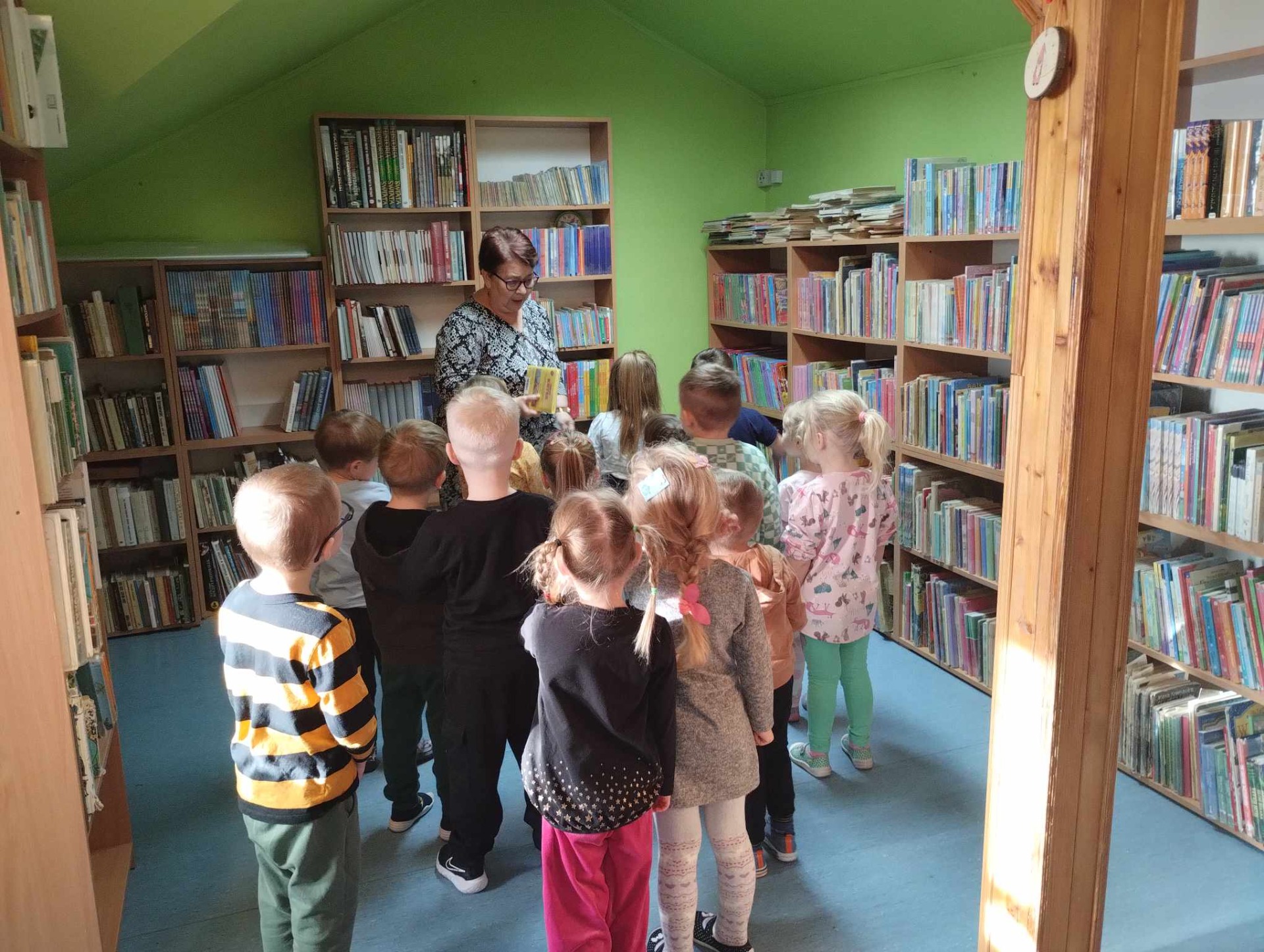 Grupa przedszkolaków zwiedza szkolną bibliotekę.