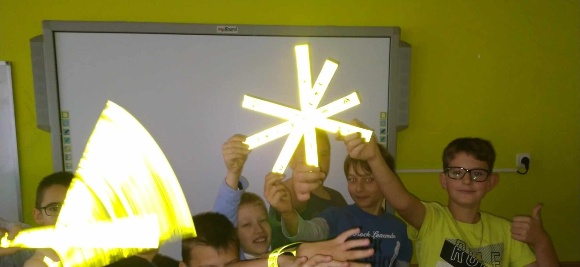 Na fotografii uczniowie klasy czwartej ułożyli odblaskową gwiazdę. Gwiazda odbija jasne światło lampy błyskowej aparatu. 